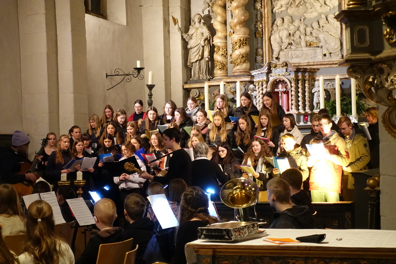 Oberstufenchor, unterstützt von David Becker (Bildmitte), im Vordergrund Schülerinnen und Schüler der Bläser-AG.